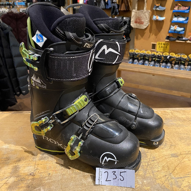 Pair of black ski boots with green accents on a wooden surface in a store setting.