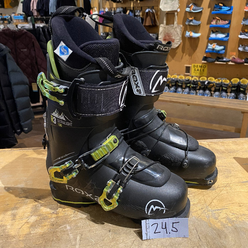 Pair of black ski boots with green buckles on a wooden surface in a store setting.