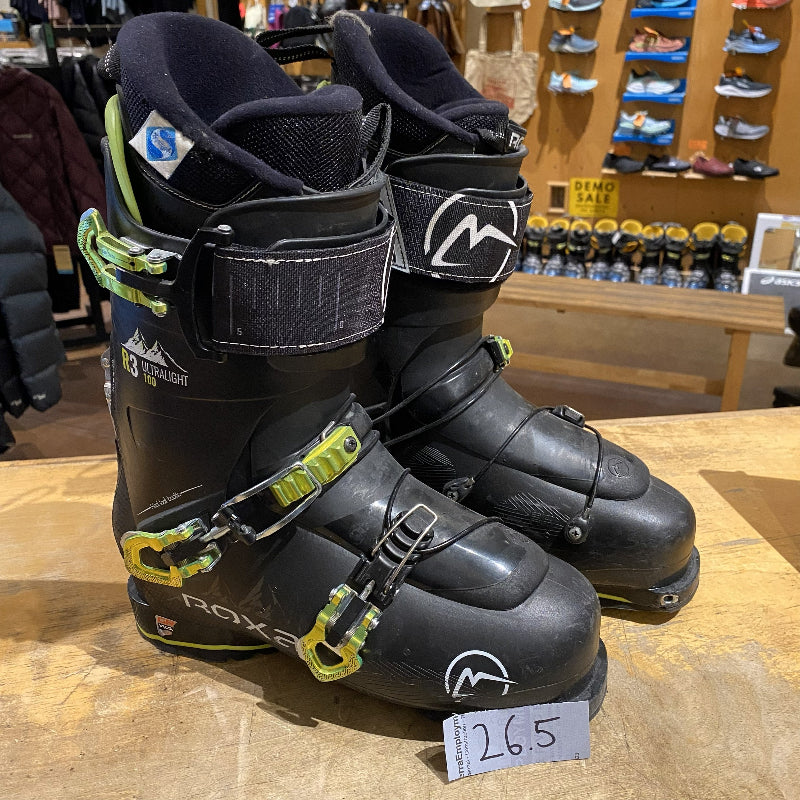 Pair of black ski boots with green accents on a wooden surface in a store setting.