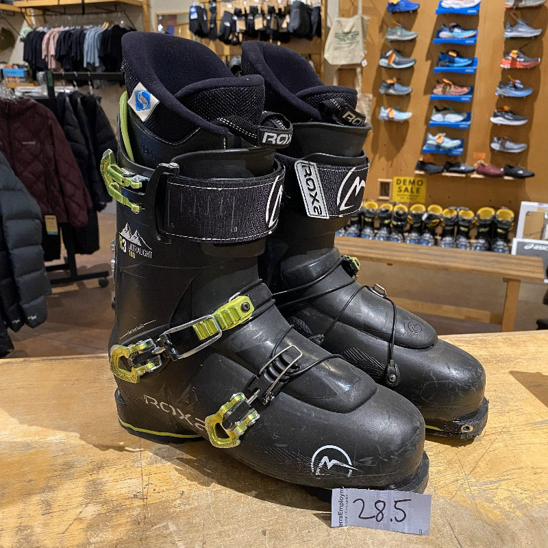 Black ski boots with green buckles on a wooden surface in a store setting.