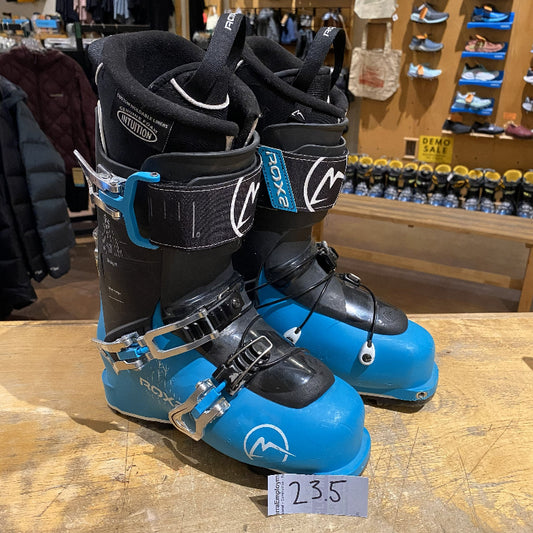 Pair of blue and black ski boots with visible brand logo on a wooden surface in a store setting.