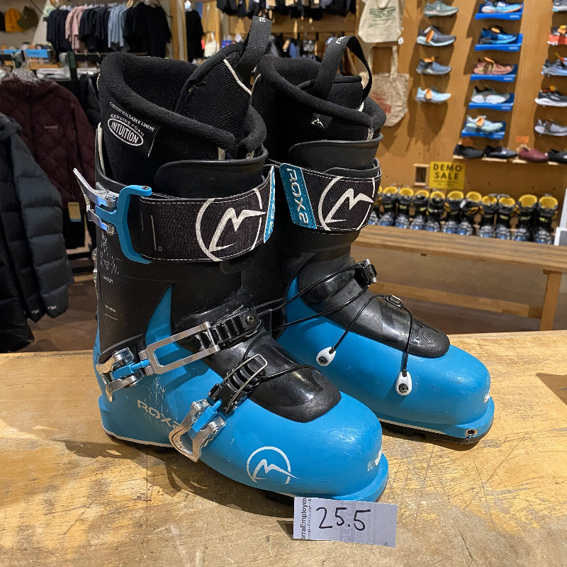 Blue ski boots with black straps on a wooden surface in a store setting.