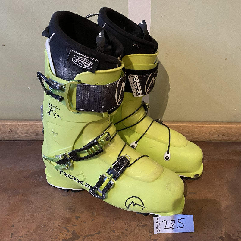 Pair of neon green ski boots with black straps on a wooden floor.