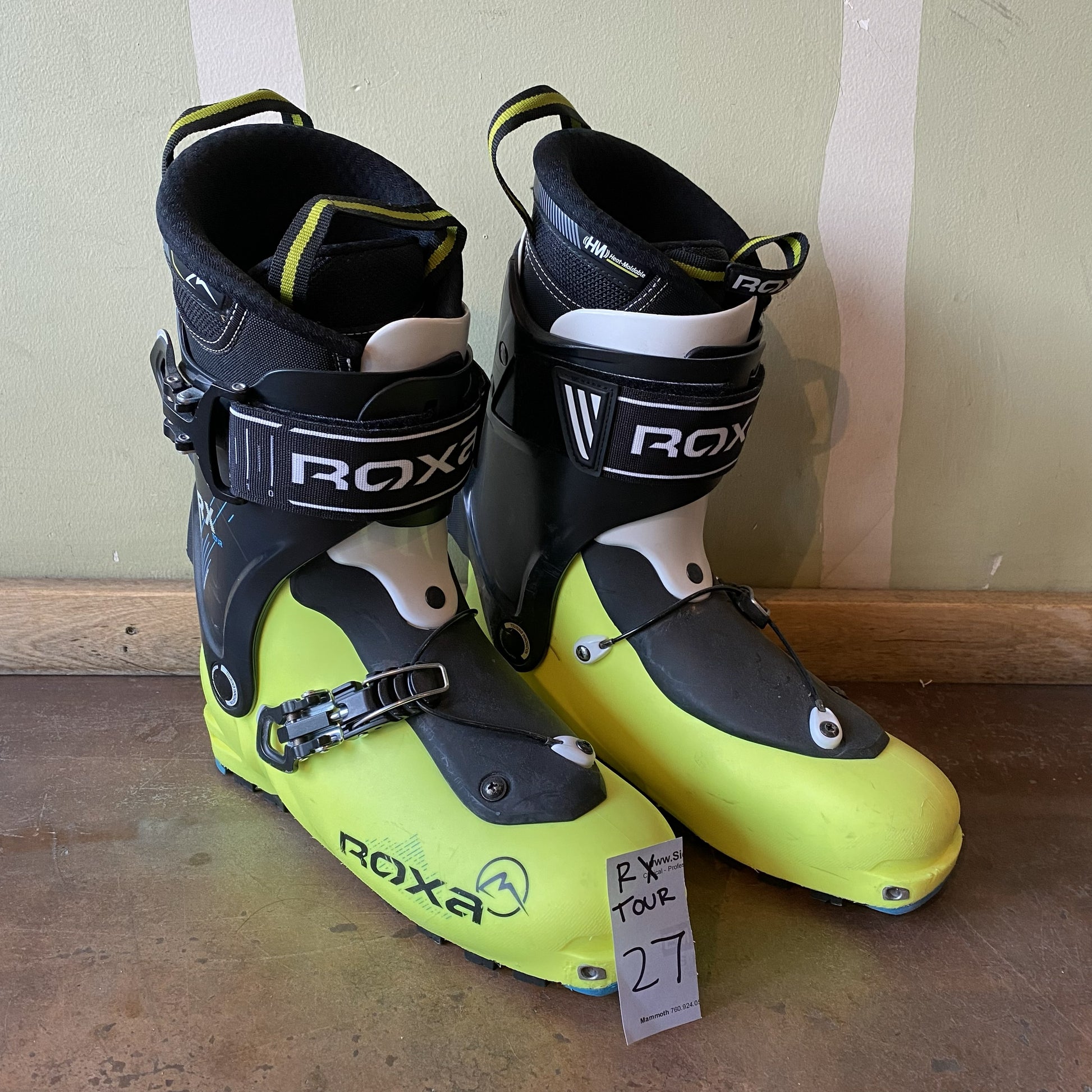 Pair of Roxa ski boots on a wooden floor with a light green wall in the background.