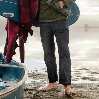 A man beside a boat holds a surfboard, wearing relaxed-fit Ripton Superlite Jeans.