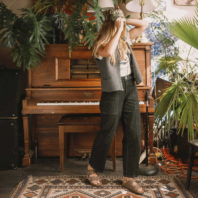 A woman poses in front of a piano, wearing Ripton Women's EZ500 Jeans, which combine comfort and durability for active use.