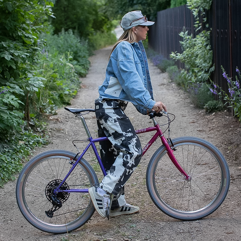 A woman biking along a dirt trail, dressed in Ripton Women's Rorschach Pants, which offer flexibility and style for active wear.