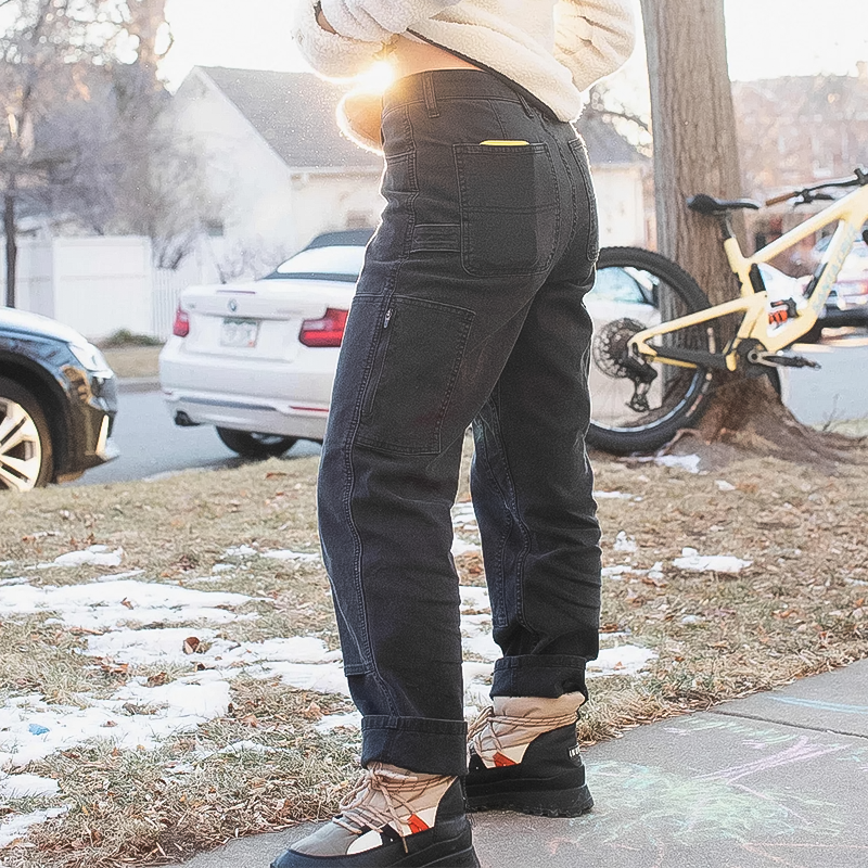 A woman in black pants and a white top stands on the sidewalk, showcasing her stylish utility jeans.