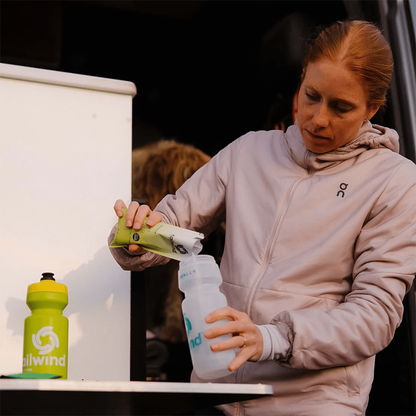 A woman pours water into a bottle to mix Lemonade Tailwind High Carb Fuel for endurance training.