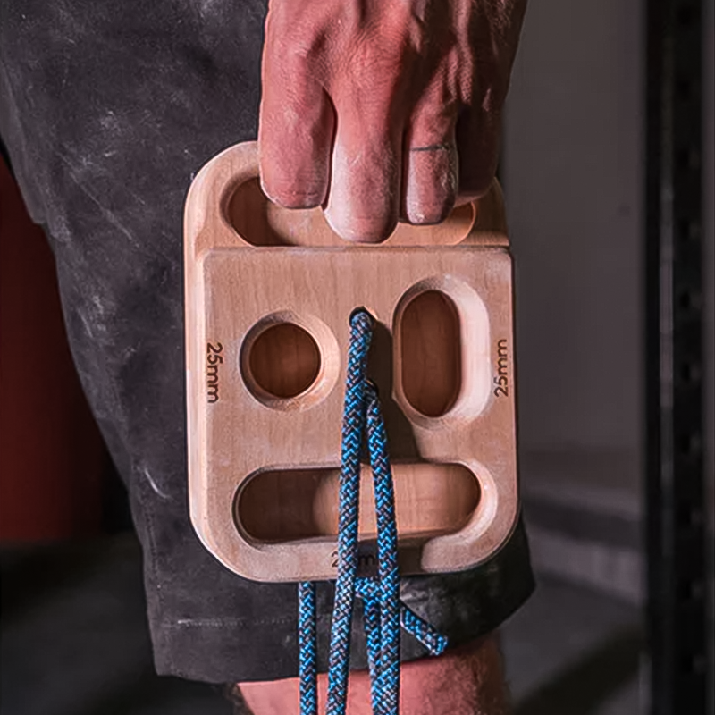 Tension Climbing The Block hangboard with climber's chalky hand, featuring multiple grip types and blue climbing rope