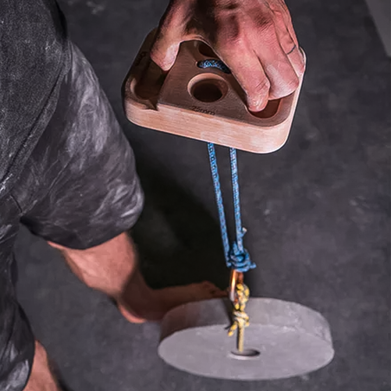 Tension Climbing hangboard with climber's hand, blue rope, and weighted pulley system for progressive training