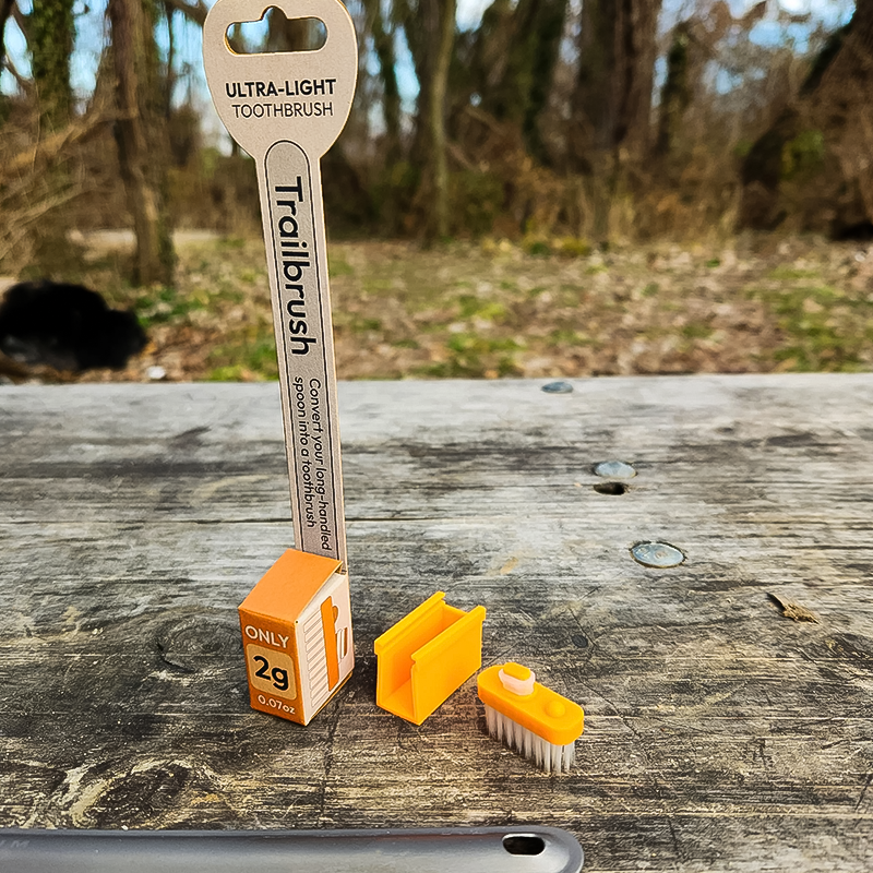 An orange compact toothbrush rest on a table, featuring the Trail Stuff Trailbrush designed for minimalistic outdoor use.