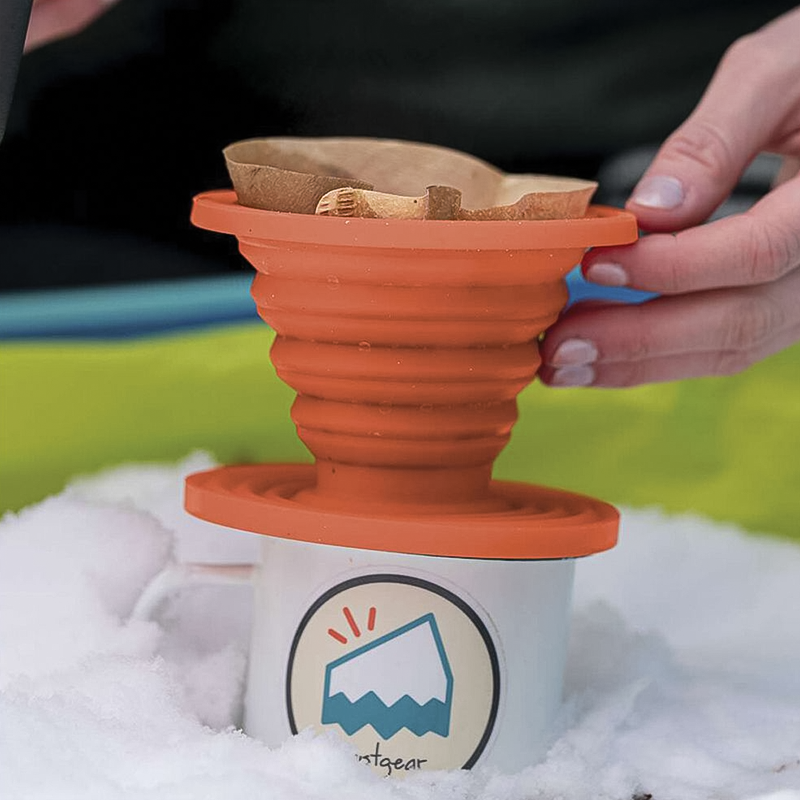 A hand holds an orange collapsible silicone coffee drip, ideal for brewing coffee on outdoor adventures.