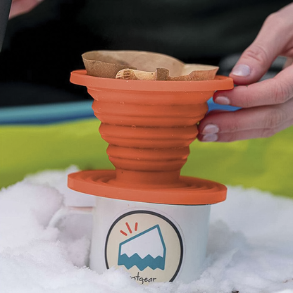 A hand holds an orange collapsible silicone coffee drip, ideal for brewing coffee on outdoor adventures.