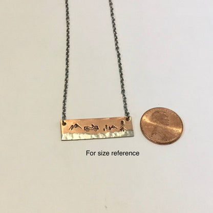 A mixed metal necklace featuring a copper bar beside a penny, showcasing hand-stamped details on an 18-inch stainless steel chain.