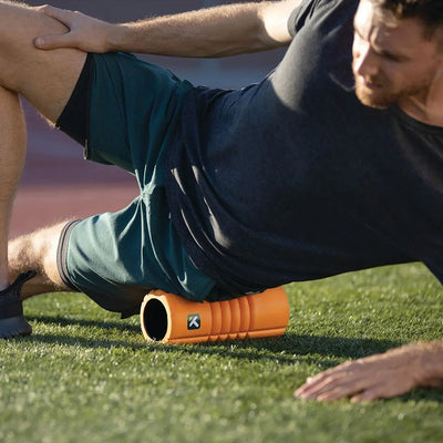 A person using the TriggerPoint Grid Travel in orange to massage his leg muscles.